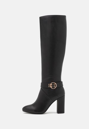 Botte en cuir noire jusqu'au genou avec talon bloc et détail de boucle circulaire dorée sur le côté.