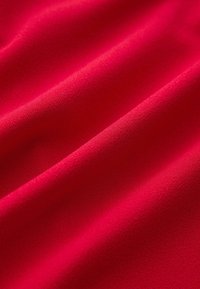 Tissu rouge vif avec une texture douce et lisse, présentant de légers plis formant des ombres et des highlights diagonaux.