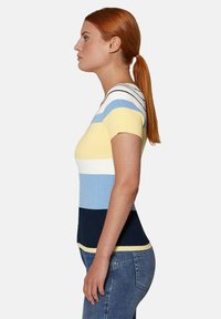 Gestreiftes Kurzarmoberteil in Gelb, Blau und Marineblau. Mit gerippter Textur und figurbetontem Design. Kombiniert mit blauen Jeans.