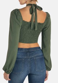 Oliven grøn cropped top med smocket bryststykke, pufærmer og sløjfebånd i ryggen. Sammen med højtaljede mørke denim jeans.