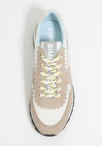 Beżowo-białe tenisówki z teksturowanego zamszu i siateczki, z zygzakowatym wzornictwem, żółtymi i fioletowymi sznurowadłami oraz czarną gumową podeszwą.