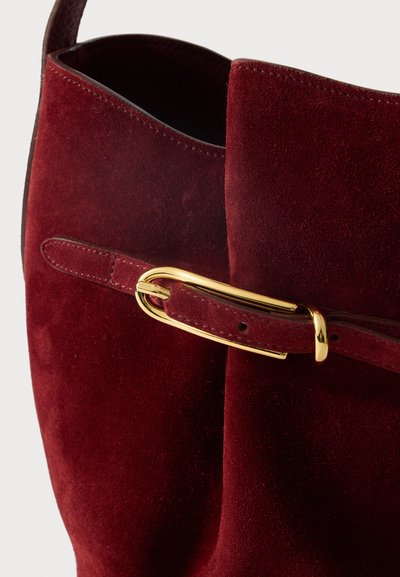 Süvendatud burgundia värvi nahast kott, millel on kuldne pandla ja rihma detail. Pehme tekstuur ja lõdva avatud ülemise disainiga.