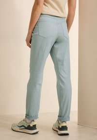 Jeans de corte ajustado en un tono azul claro con dobladillos acampanados y dos bolsillos traseros, combinados con zapatillas de color verde grisáceo con una suela moteada.