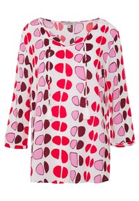 Blouse blanche avec un décolleté en V et des manches 3/4. Présente un motif de formes rouges, roses et bordeaux. Cordons avec des pompons au niveau du col.