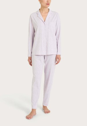 Donna che indossa un pigiama a maniche lunghe di colore viola chiaro con bottoni e pantaloni abbinati con un motivo sottile su tutta la superficie, in piedi a piedi nudi.