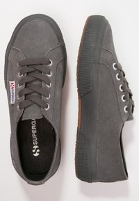 Grå mockaskor med rund tå, snörning fram, gummisula och texturerade bruna accenter. Sidologga och metalliska snörhål synliga.