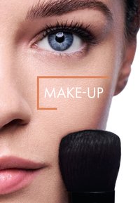 Nahaufnahme eines Gesichts mit klarer Haut. Ein schwarzer Makeup-Pinsel berührt die Wange, hervorgehoben von einem lebendigen blauen Auge daneben.