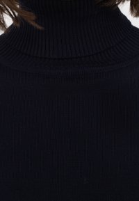 Dunkelblauer gerippter Rollkragenpullover mit hohem Kragen. Der Stoff hat eine glatte Textur, die das gestrickte Muster und das figurbetonte Design zur Geltung bringt.