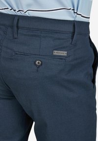 Pantalon bleu marine avec un tissage texturé, doté d'une fermeture à bouton et d'une petite étiquette de marque près de la poche arrière.