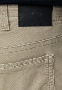 Beige corduroy broek met een gestructureerd oppervlak, voorzien van een zwart leren label met de tekst "s.Oliver" op de tailleband en contrasterende stiksels.