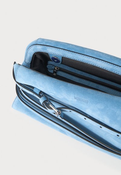 Sac à épaule en daim bleu clair avec intérieur noir, poche zippée et détail boucle métallique.