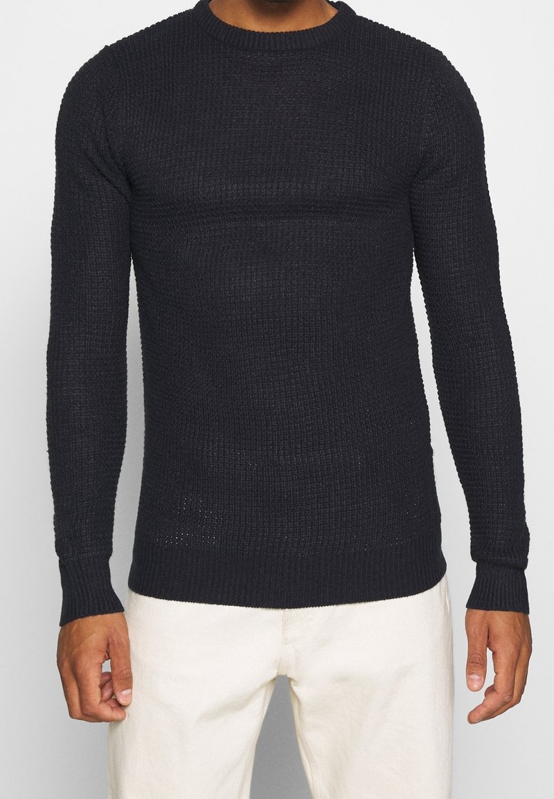 Svart stickad tröja med långa ärmar och rund halsringning, med en texturerad mönstring och ribbade muddar och nederkant.