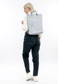Lichtgrijze tote-stijl rugzak met een bovenhandvat, een platte voorzak en een contrasterende groene streep. Gemaakt van duurzaam materiaal, met een gestructureerd ontwerp.