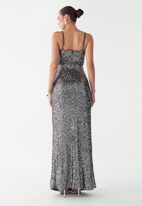 Pikk, vormiv õhtukleit mustade ja hõbedaste litritega, õhukeste rihmadega ning volditud helmestega, millel on sile ja läikiv tekstuur.