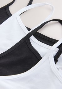 Two black and white tank tops with thin straps, layered overlapping on a light background.