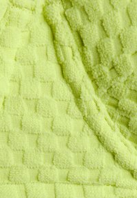 Tecido verde limão com uma superfície suave e texturizada, apresentando um padrão de tabuleiro de xadrez elevado e seções lisas intercaladas.