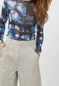 Maglietta a maniche lunghe con un motivo floreale multicolore su uno sfondo scuro, abbinata a pantaloni beige chiaro a vita alta con ampie tasche.