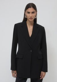 Black blazer with a structured design, single button closure, notch lapel, and two front pockets. Smooth fabric and tailored fit.