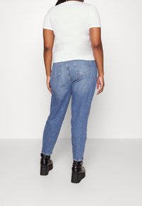 Vit t-shirt med kort ärm i kombination med ljusblå jeans med avslappnad passform och två bakfickor, kompletterad med svarta platåstövlar.