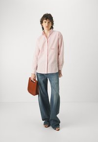 Camicia a righe rosse e bianche con maniche lunghe, abbinata a jeans a gamba larga blu e una borsa marrone. Sandali piatti completano il look.