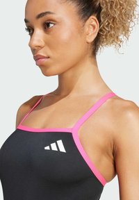 Zwarte sporttop met dunne roze bandjes, voorzien van een wit logo ontwerp aan de linkerkant. Gladde textuur, aansluitend ontwerp.