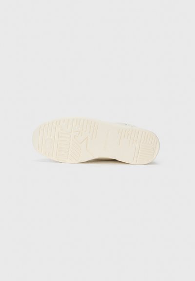 Semelle en crème de sneaker avec caoutchouc texturé pour une meilleure adhérence. Présente des motifs striés et un logo en relief sur la surface inférieure.