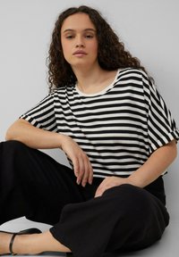 Zwart-wit gestreepte T-shirt met een ronde hals, korte mouwen en een losse pasvorm. Gekenmerkt door losse zwarte broeken.