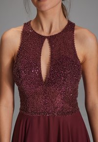 Robe bordeaux avec un bustier orné de perles présentant un décolleté en trou de serrure ; jupe fluide tombant élégamment à partir de la taille cintrée.