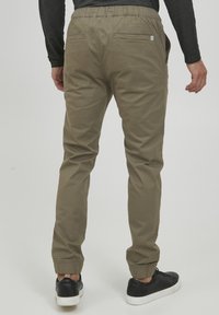 Khaki joggers met elastische tailleband, twee achterzakken en taps toelopende boorden. Gecombineerd met zwarte sneakers met witte zolen.
