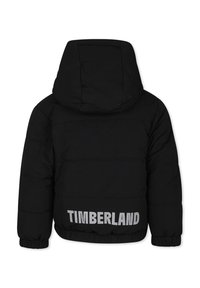 Doudoune noire avec capuche, dotée d'un design cousu et de poignets élastiqués. Affiche le logo "TIMBERLAND" en gris au dos.