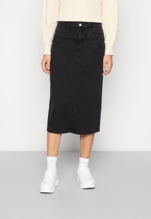 Sort knælange denimnederdel med forlommer, båret med hvide sneakers og hvide crew-sokker mod en ensfarvet baggrund.