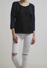 Svart texturerad topp med korta marinblå ärmar, tillsammans med vita slitna skinny jeans med hål vid knäna. Enkelt design och figurnära siluett.