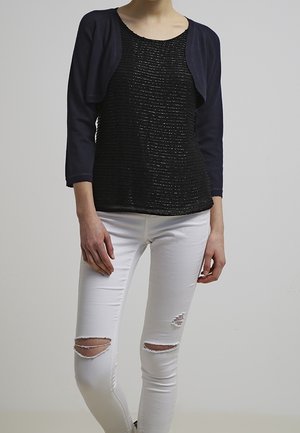 Top nero con texture e maniche corte blu navy, abbinato a jeans skinny bianchi strappati con strappi sulle ginocchia. Design semplice e silhouette aderente.
