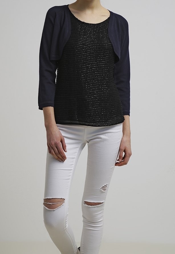 Svart texturerad topp med korta marinblå ärmar, tillsammans med vita slitna skinny jeans med hål vid knäna. Enkelt design och figurnära siluett.