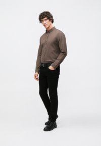 Braunes Langarmhemd mit Button-Down-Kragen, kombiniert mit schwarzen Slim-Fit-Hosen und schwarzen Schnürstiefeln, mit einfachem Design und einfarbigen Farben.