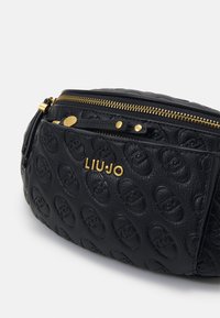 Geantă din piele texturată neagră cu un model logo embosat, accente din hardware aurie și închidere cu dublu fermoar. Include un ciucure detașabil.