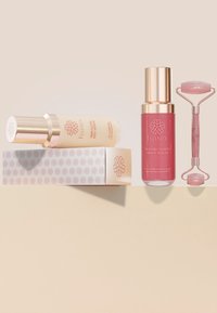 Due fiale di siero per la cura della pelle in eleganti bottiglie, una rosa e una trasparente, con dettagli dorati; un rullo di giada rosa affiancato a una scatola decorata.