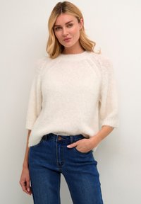 Maglione lavorato a maglia morbido color crema con maniche raglan e polsini a coste larghi, abbinato a jeans in denim blu a vita alta.