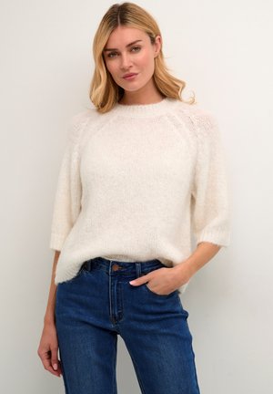 Pull en tricot moelleux de couleur crème avec des manches raglan et de larges poignets côtelés, associé à un jean en denim bleu taille haute.