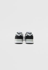Schwarz-weiße Sportschuhe mit strukturiertem Finish, das ein elegantes Design und eine niedrige Profilhöhe aufweist, akzentuiert durch eine hellfarbige Sohle.