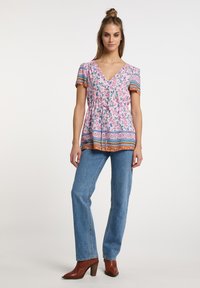 Blomstret pink bluse med korte ærmer, bindebånd i taljen og mønstret kant; parret med blå denimjeans og brune hæle støvler.