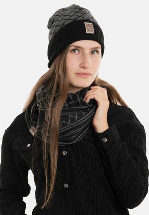 Zwarte gebreide beanie met een geometrisch patroon en een merkembleem; bijpassende zwarte sjaal met patroon om de nek gewikkeld; gestructureerde stof.
