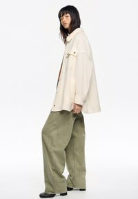 Camisa de lana mezclada en crema con cuello, un bolsillo en el pecho y pantalones de pierna ancha verdes con una textura suave y una cintura alta. Botas negras.