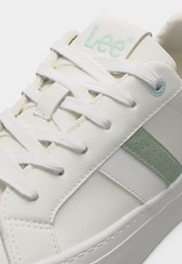 Λευκό χαμηλό αθλητικό παπούτσι με λευκά κορδόνια, ανοιχτοπράσινη πλευρική ρίγα και το λογότυπο "Lee" στη γλώσσα με ανοιχτοπράσινο κείμενο.