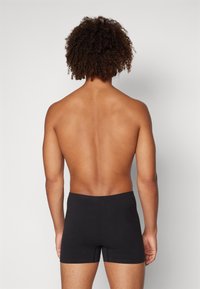Schwarze Boxerbriefs aus weichem Stoff, mit einem nahtlosen Bund und einer engen Passform, von hinten vor einem neutralen Hintergrund betrachtet.