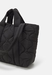 Czarna, pikowana torba na ramię z teksturowanymi uchwytami, charakteryzująca się gładką powierzchnią i wyściełanym wyglądem. Wzmocnione boczne szwy dodają struktury.