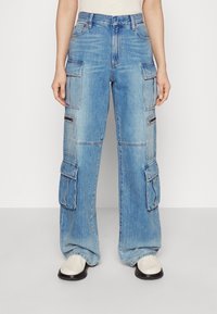 Vaaleansiniset cargo-farkut löysällä istuvuudella, useilla taskuilla ja näkyvillä ompeluyksityiskohdilla. Valmistettu farkkukankaasta, jossa on haalistunut pesupinta.