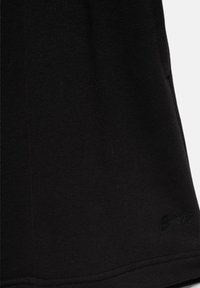Tissu noir avec un logo embossé subtil près du bord inférieur, montrant la texture et les détails de couture.
