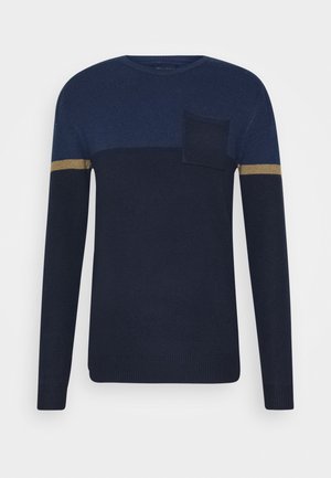 Granatowy sweter z dzianiny z długim rękawem, z jaśniejszą częścią na górnej części klatki piersiowej i jedną kieszenią na piersi, z beżowym paskiem na każdym rękawie.