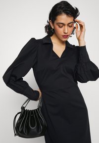 Vestido preto com mangas bufantes, decote em V e corpete estruturado. Acompanhado de uma bolsa de cordão em couro preto com detalhes em prateado.